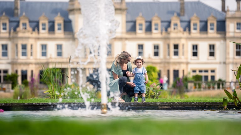 A mother and toddler watching the fountain at Dyffryn Gardens, Dyffryn House is in the background.